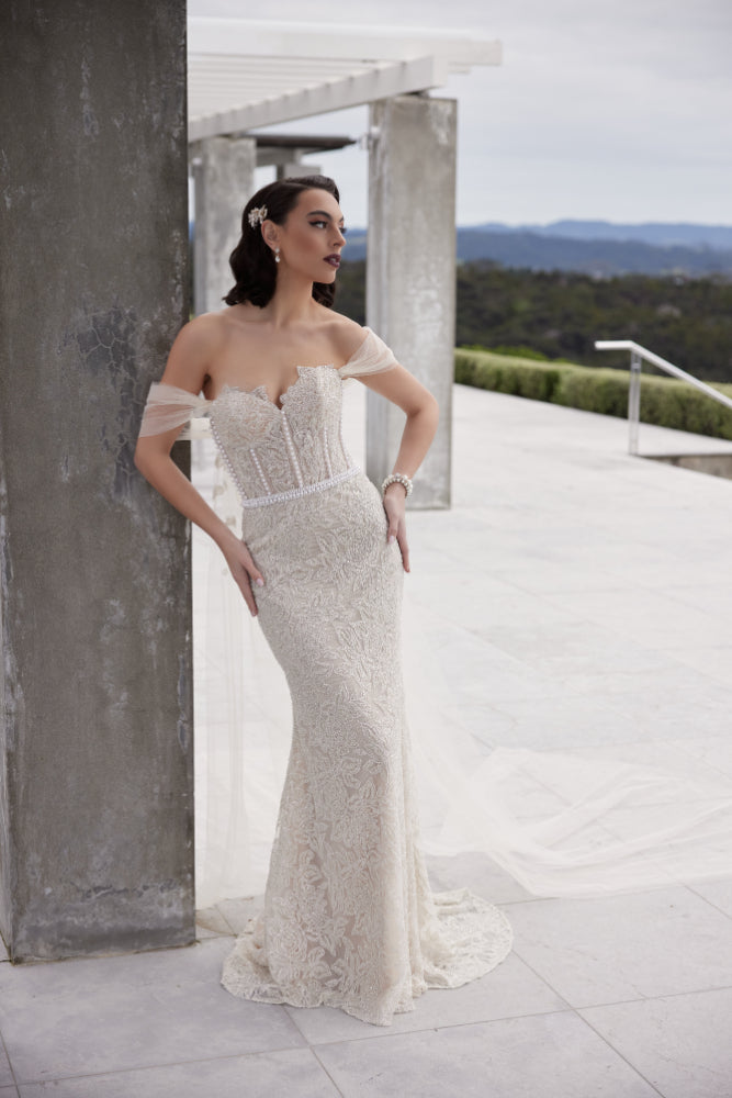 Tristan gown in champagne beading with pearl columns and waistband. Decorative tulle sleeves that flow into wings. Sweetheart strapless bodice and sheath silhouette.