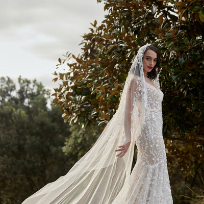 Noor gown with champagne lining and 3D floral ivory lace overlay. Mermaid silhouette with champagne satin waistband. Veil decorated with 3D flowers over the head with a soft tulle train.