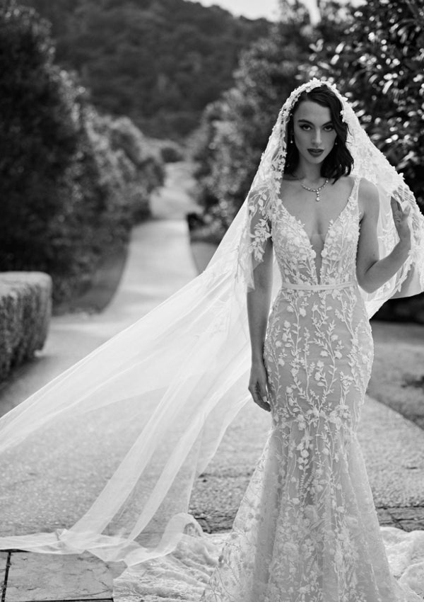 Black and white photo of Noor gown with veil. Mermaid silhouette with 3D floral lace and plunging v-neckline.