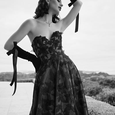 Black and white image of Tokyo gown. Floral textured organza sits over glitter tulle in this sweetheart bodice, a-line gown. Model wears black satin gloves with bows.