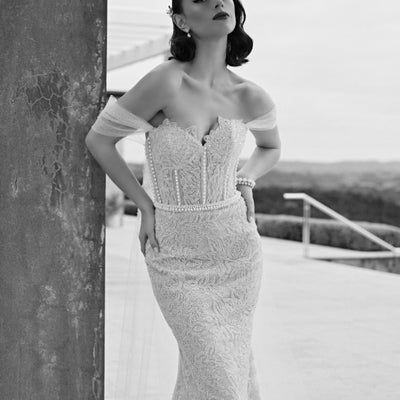 Black and white image of Tristan gown in champagne beading with pearl columns and waistband. Decorative tulle sleeves that flow into wings. Sweetheart strapless bodice and sheath silhouette.