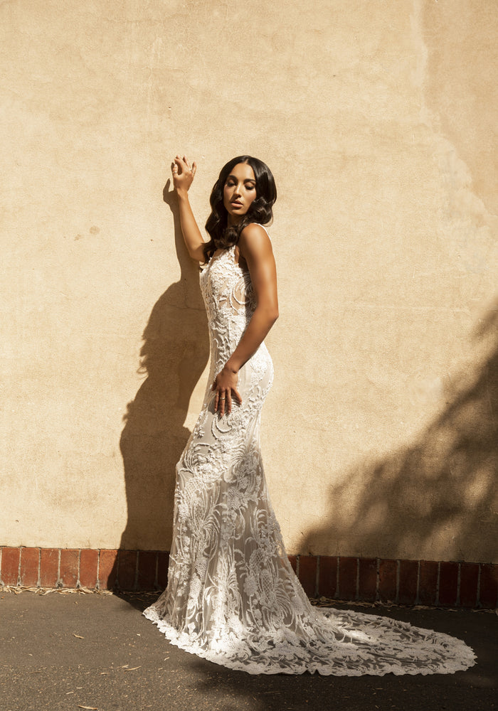 Side view of Nikola gown in fully-beaded lace on a fit-n-flare silhouette. Beaded train.
