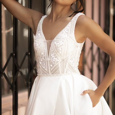 Ivory Raven gown with plunging v-neckline and dramatic a-line skirt with split. Bodice features geometric bead work and small mesh panel over bust for modesty.