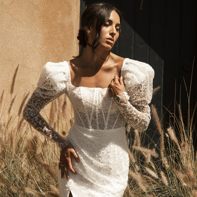 Fully beaded Rachel gown with sheer mutton sleeves and visible boning through the bodice. The ruched skirt is lined in ivory with asplit over the right leg.