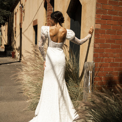 Back view of Rachel gown. Scoop back with fit-n-flare silhouette. Mutton sleeves and visible boning through the bodice.
