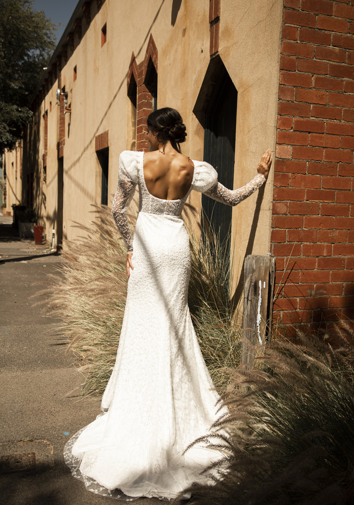 Back view of Rachel gown. Scoop back with fit-n-flare silhouette. Mutton sleeves and visible boning through the bodice.