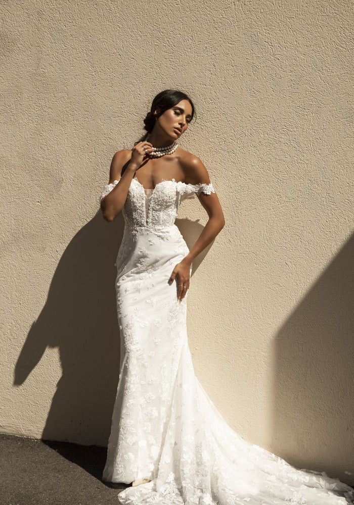 Roberta dress featuring a fit-n-flare silhouette with a plunging sweetheart neckline and off the shoulder straps. A structured bodice with floral lace through the entire gown.