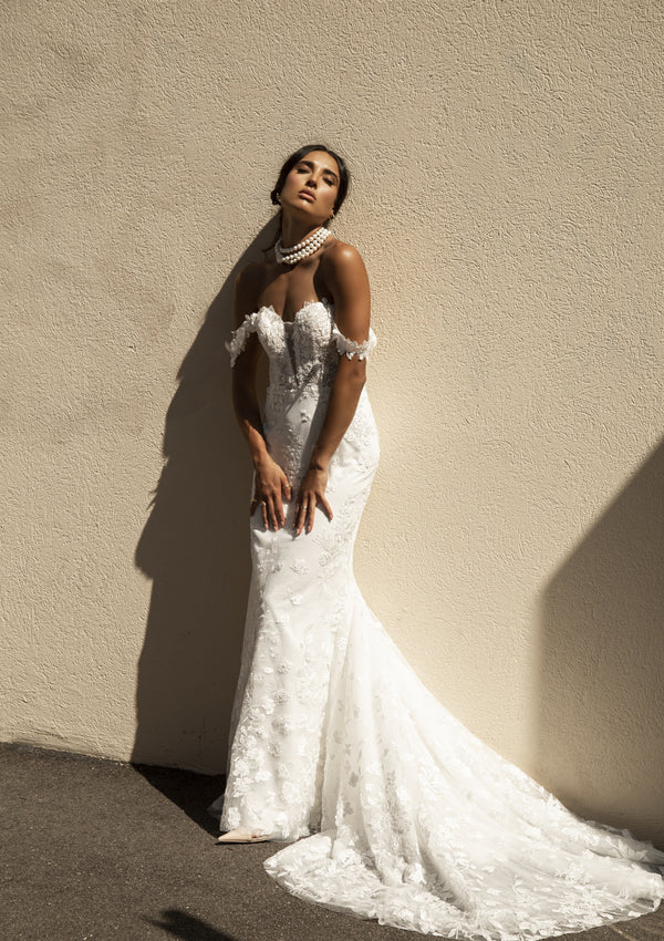 Roberta dress featuring a fit-n-flare silhouette with a plunging sweetheart neckline and off the shoulder straps. A structured bodice with floral lace through the entire gown.
