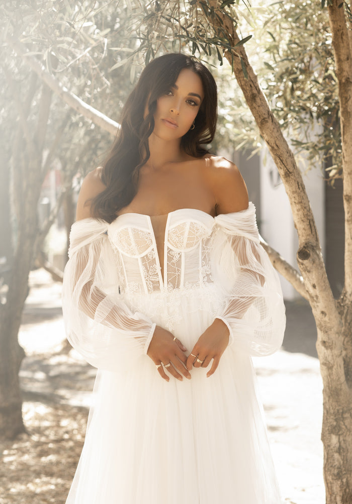 Soft ivory tulle dress with plunging sweetheart neckline and sheer boned corset. Decorated with ruched tulle and beaded lace. She also features pleated tulle detachable sleeves.