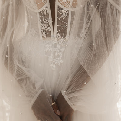 Close up of Riese dress bodice. Plunging sweetheart neckline with beaded lace and ruched tulle detail. Styled with pearl veil.