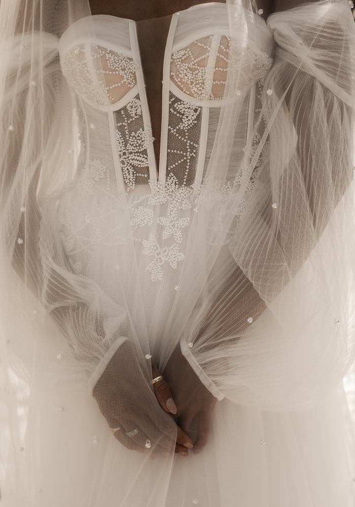 Close up of Riese dress bodice. Plunging sweetheart neckline with beaded lace and ruched tulle detail. Styled with pearl veil.