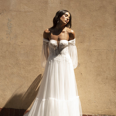 Soft ivory tulle dress with plunging sweetheart neckline and sheer boned corset. Decorated with ruched tulle and beaded lace. She also features pleated tulle detachable sleeves. Tiered tulle a-line skirt.