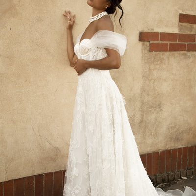 Side view of Rohini dress with soft tulle off-the-shoulder sleeves and textured applique on a soft tulle a-line skirt. 