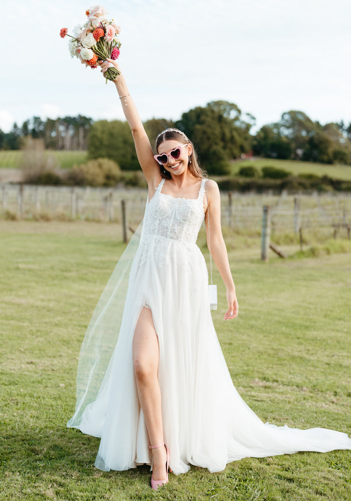 Namesake bride Frankie wears Frankie dress. She wears pink shoes, loveheart sunglasses and holds a colourful bouquet in the air..